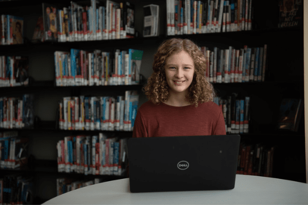 Teen girl using laptop in library