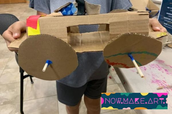 Child holding a cardboard creation with cardboard wheels