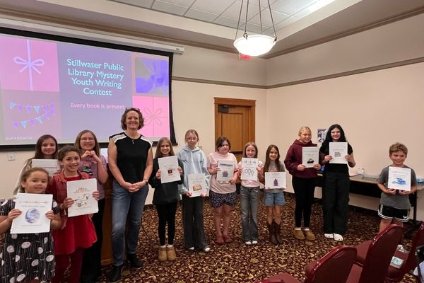 Twelve youth writers, ages 8-12, posing for a picture with author Rebecca Ansari in the library's Margaret Rivers meeting room